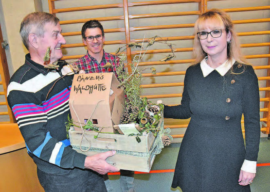 Hüttenwart für 26 Jahre Betreuung der Holziker Waldhütte geehrt: Lukas Treier (Bildmitte) überreichte Ueli Hunziker einen Geschenkkorb mit Miniaturwaldhütte, rechts Frau Gemeindeammann Jacqueline Hausmann. (Bild: aw.)